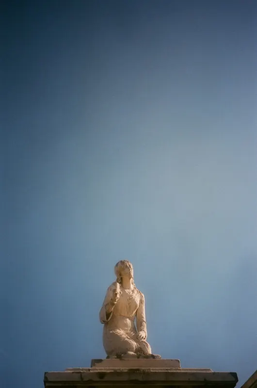 A kneeling stone statue on a pedestal against a deep blue sky