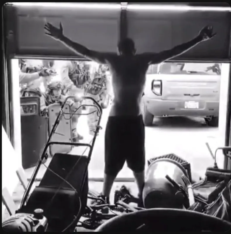 A shirtless man standing with his arms outstretched in a garage doorway, facing armed police