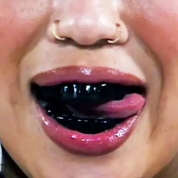 Close-up of glossy lips, a double nose ring and a black grill over the teeth